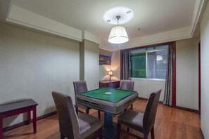 A room with a pool table, four chairs, a lamp, a window with curtains, and a ceiling light fixture.