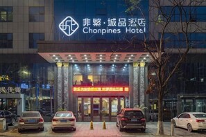 L’entrée d’un hôtel, avec une enseigne indiquant « Hôtel Chonpines », et plusieurs voitures garées devant.