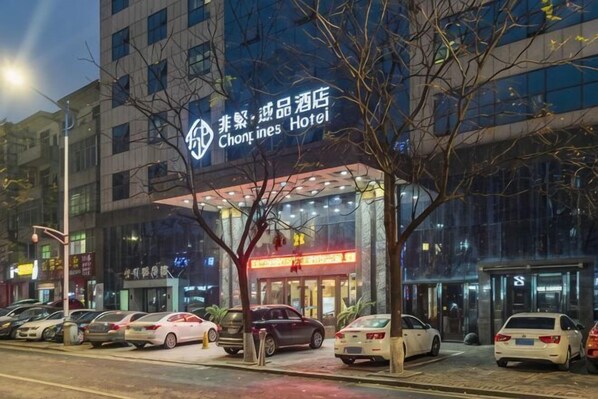 A hotel with a modern facade, a visible entrance, and a parking lot with several cars.