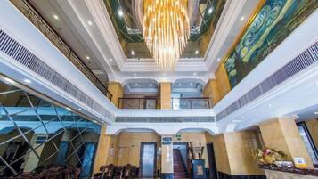 A hotel lobby with a grand chandelier, a staircase, and a reception desk.