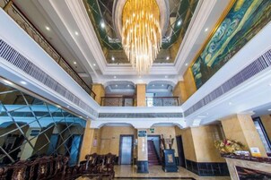 Un vestíbulo de hotel con una gran araña, una escalera y un mostrador de recepción.