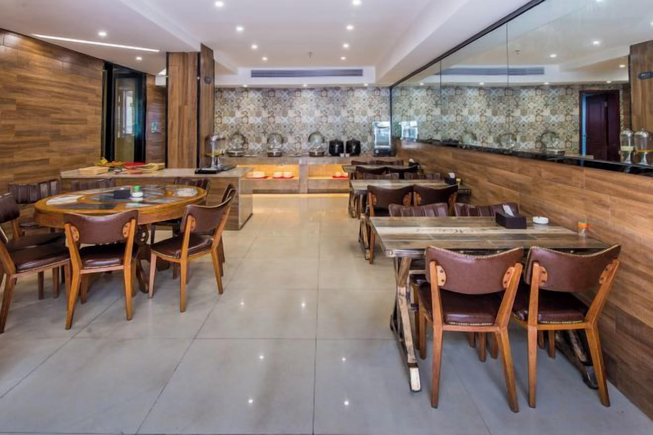 A modern dining area with round tables and chairs, a kitchen in the background, and a polished floor.
