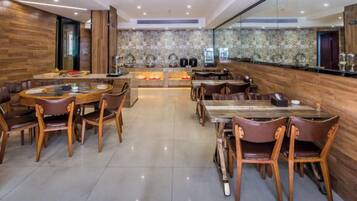 A modern dining area with round tables and chairs, a kitchen in the background, and a polished floor.