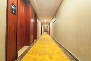 Pasillo de hotel con puertas de madera, alfombra amarilla y un cartel que indica disponibilidad de habitaciones.