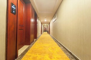 Pasillo de hotel con puertas de madera, alfombra amarilla y un cartel que indica disponibilidad de habitaciones.