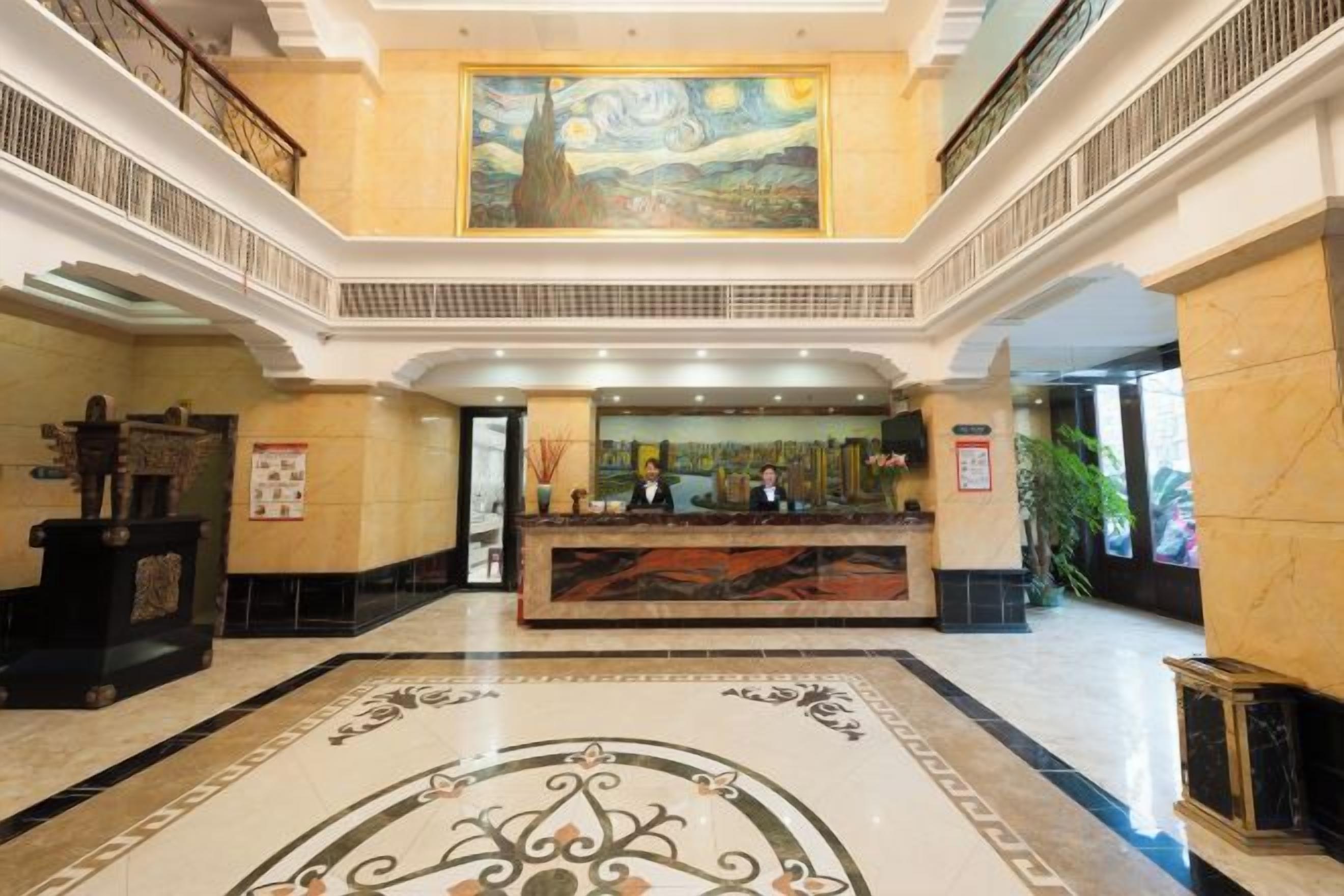 A hotel lobby with a reception desk, a large painting on the wall, and a marble floor.