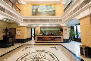 Um saguão de hotel com uma recepção, um quadro grande na parede e piso de mármore.