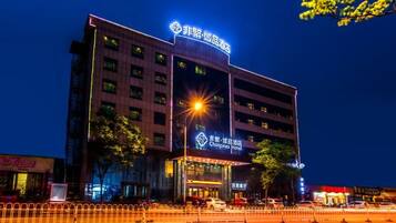 A multi-story hotel building with illuminated signage, a prominent entrance, and a parking area in front.