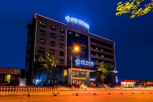 Un hotel de varios pisos con señalización iluminada, una entrada destacada y un estacionamiento al frente.