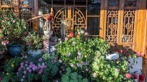 A traditional wooden building with intricate lattice windows and a garden with various plants and flowers. - Erquan Inn Ancient city (Lijiang)