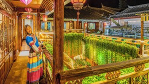 A traditional Chinese building with wooden architecture, a person in traditional attire, and a well-lit interior. - Erquan Inn Ancient city (Lijiang)