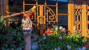 A traditional wooden building with intricate lattice windows and a bird sculpture in the garden. - Erquan Inn Ancient city (Lijiang)
