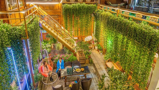 An indoor atrium with a central staircase surrounded by lush greenery and wooden railings. - Erquan Inn Ancient city (Lijiang)