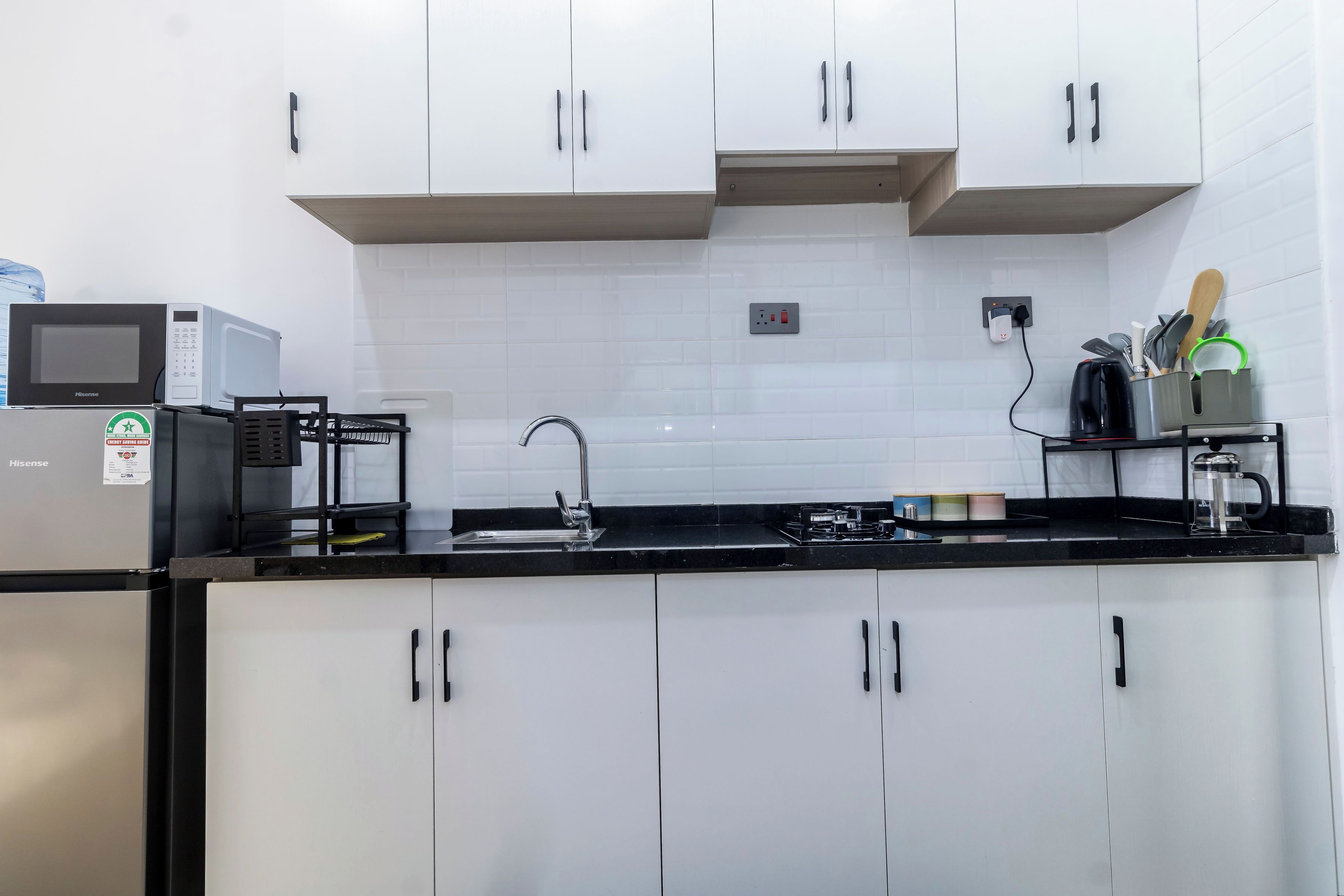 Una cocina moderna con armarios blancos, encimera negra, microondas, fregadero y cafetera.