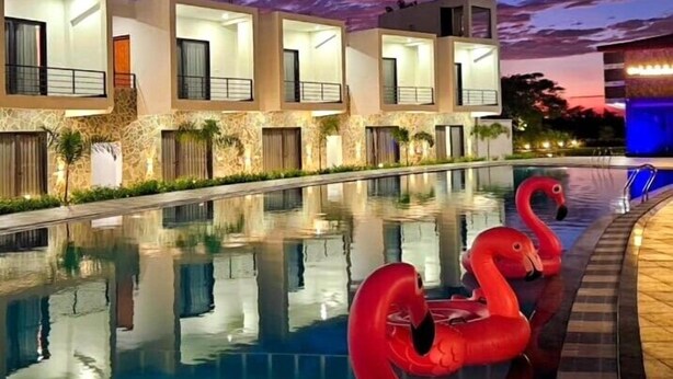 Une piscine avec des bouées en forme de flamants roses, un bâtiment moderne doté de balcons et un ciel crépusculaire.