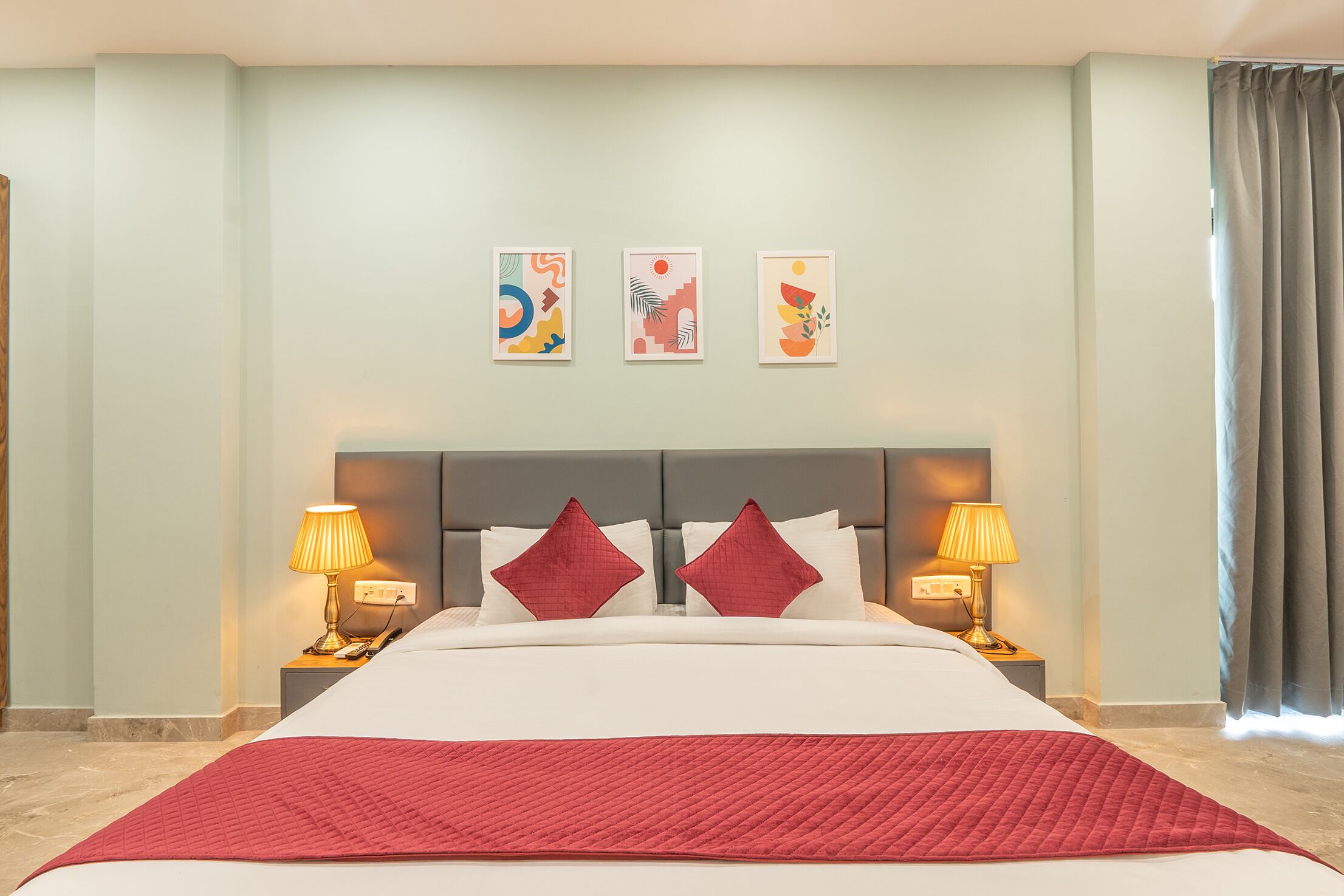 A hotel room with a large bed, two bedside lamps, a headboard, and three wall art pieces.