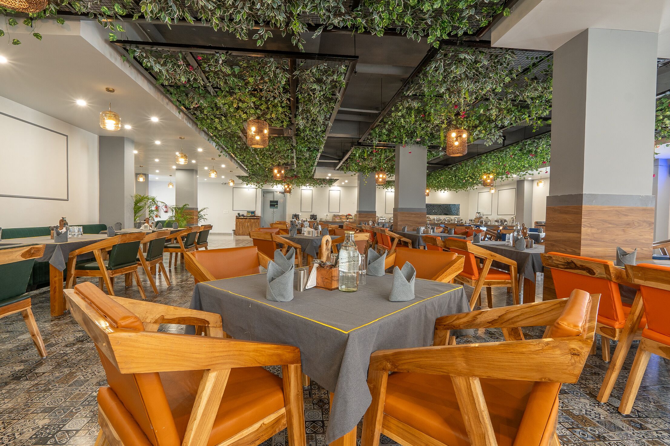 A spacious conference room with round tables, wooden chairs, and green plants hanging from the ceiling.