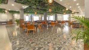 Un vaste espace intérieur doté d’un sol à motifs, de tables et de chaises en bois, de luminaires suspendus et de plantes vertes fixées au plafond.
