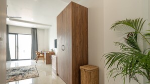 Un hall d’hôtel moderne avec un séparateur en bois, un tabouret en osier, une grande plante en pot et une vue sur la salle à manger.