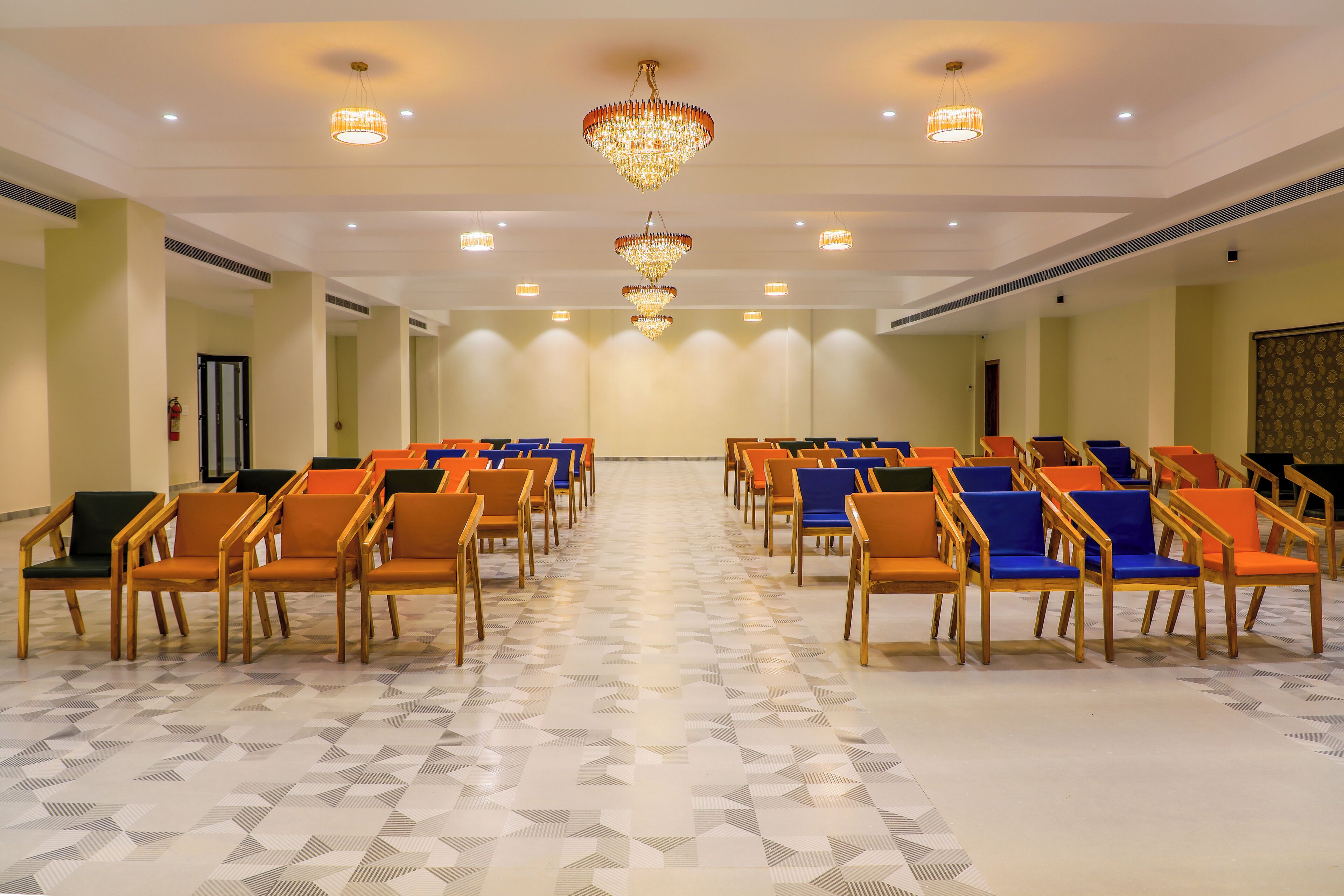 Un salón de conferencias con filas de sillas de madera y cojines azules, suelo estampado y una araña.