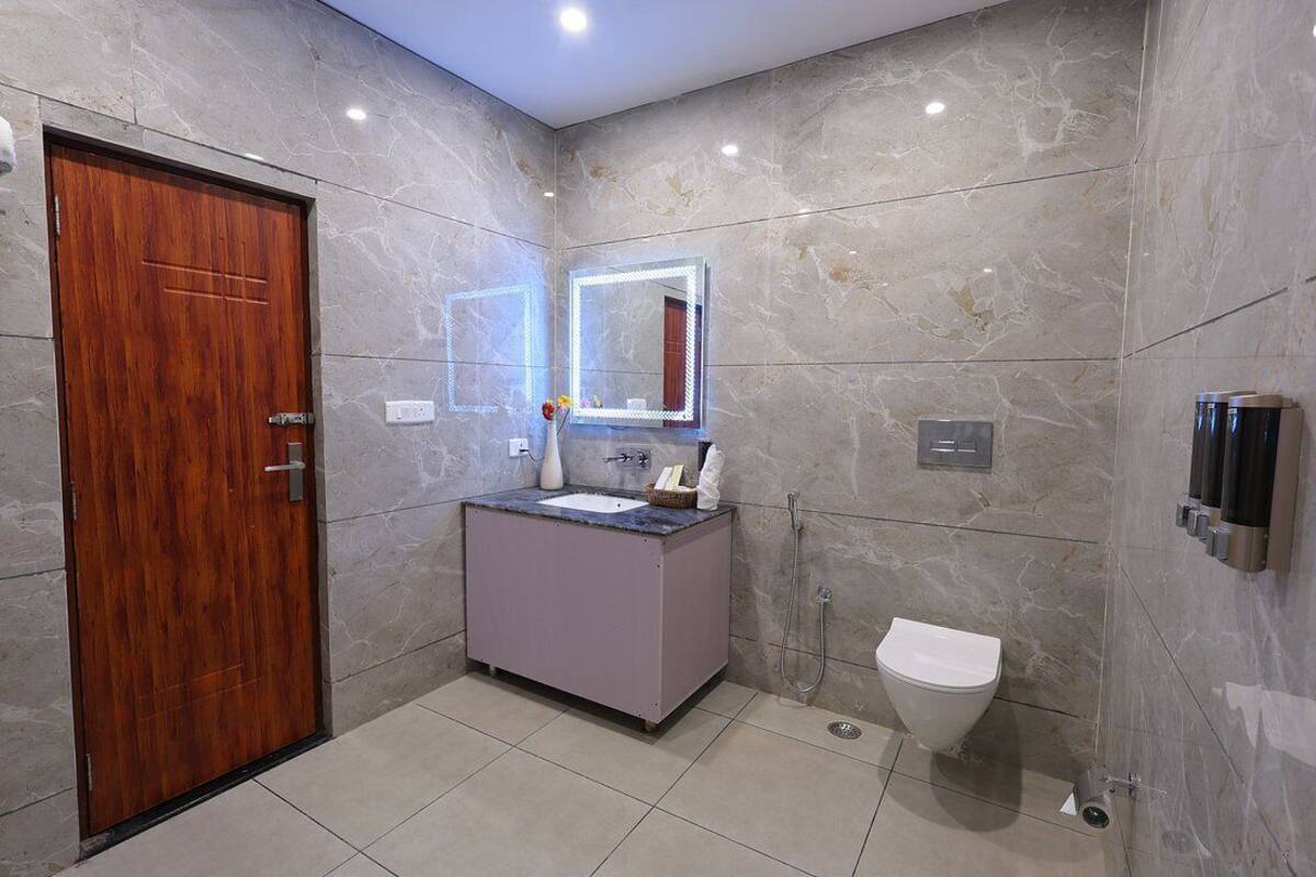 A modern bathroom with a marble wall, a wooden door, a vanity with a mirror, a toilet, and a shower.