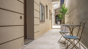 A corridor with a door, a potted plant, and two metal-framed tables with chairs.