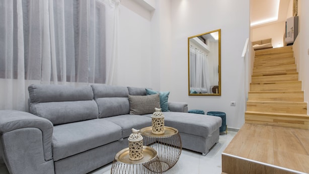 A modern living room with a grey sofa, two decorative side tables, a mirror, and a wooden staircase.