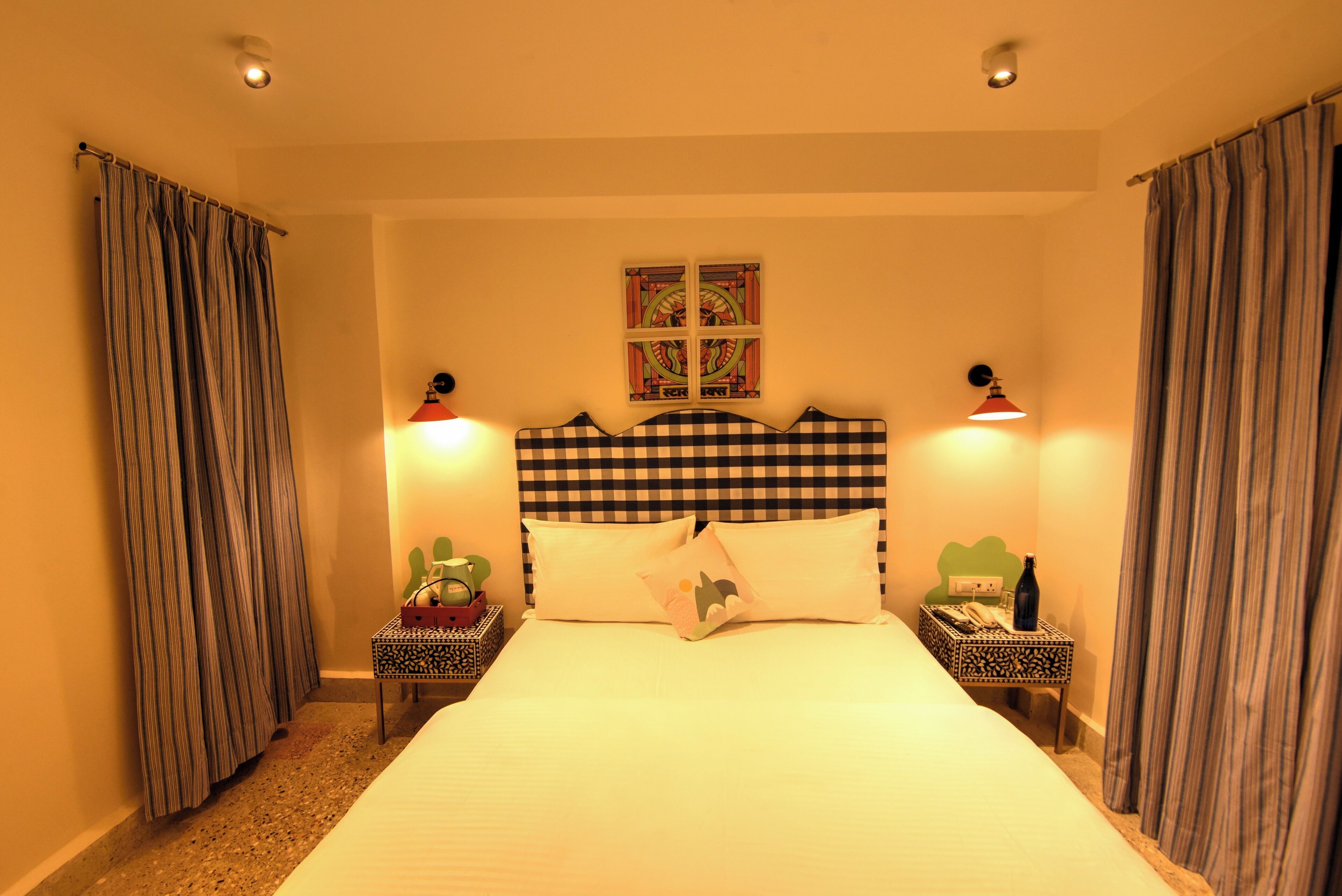 A hotel room with a checkered headboard, two bedside tables with lamps, a bed with pillows, and curtains on both sides.