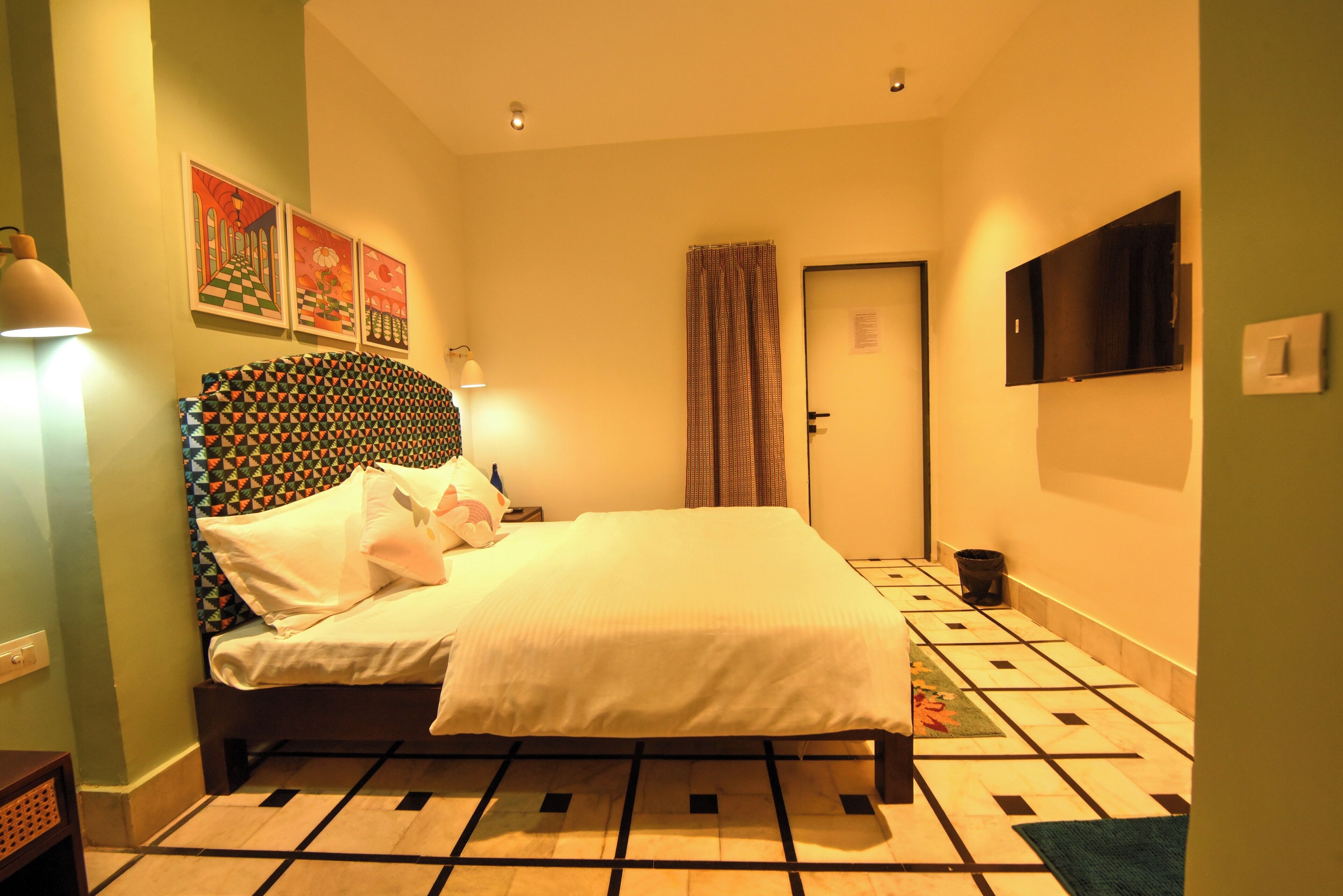 Un dormitorio ordenado con cama, mesita de noche, lámpara y televisor montado en la pared.