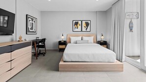 Une chambre moderne avec un lit, un bureau et une chaise, une télévision et des œuvres d’art accrochées aux murs.