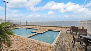 Un área de piscina con muelle de madera, sillas de descanso y cerca blanca.
