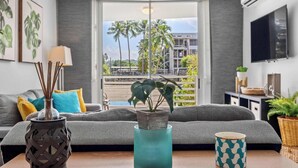 Una sala moderna con un sofá gris, un florero verde azulado con una planta y una taza estampada sobre una mesa de madera.