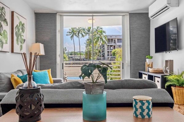 A modern living room with a grey sofa, a teal vase with a plant, and a patterned mug on a wooden table.