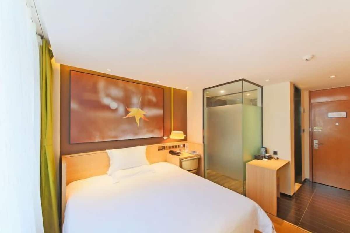 A hotel room with a bed, a nightstand, a desk, a mirror, and a door.