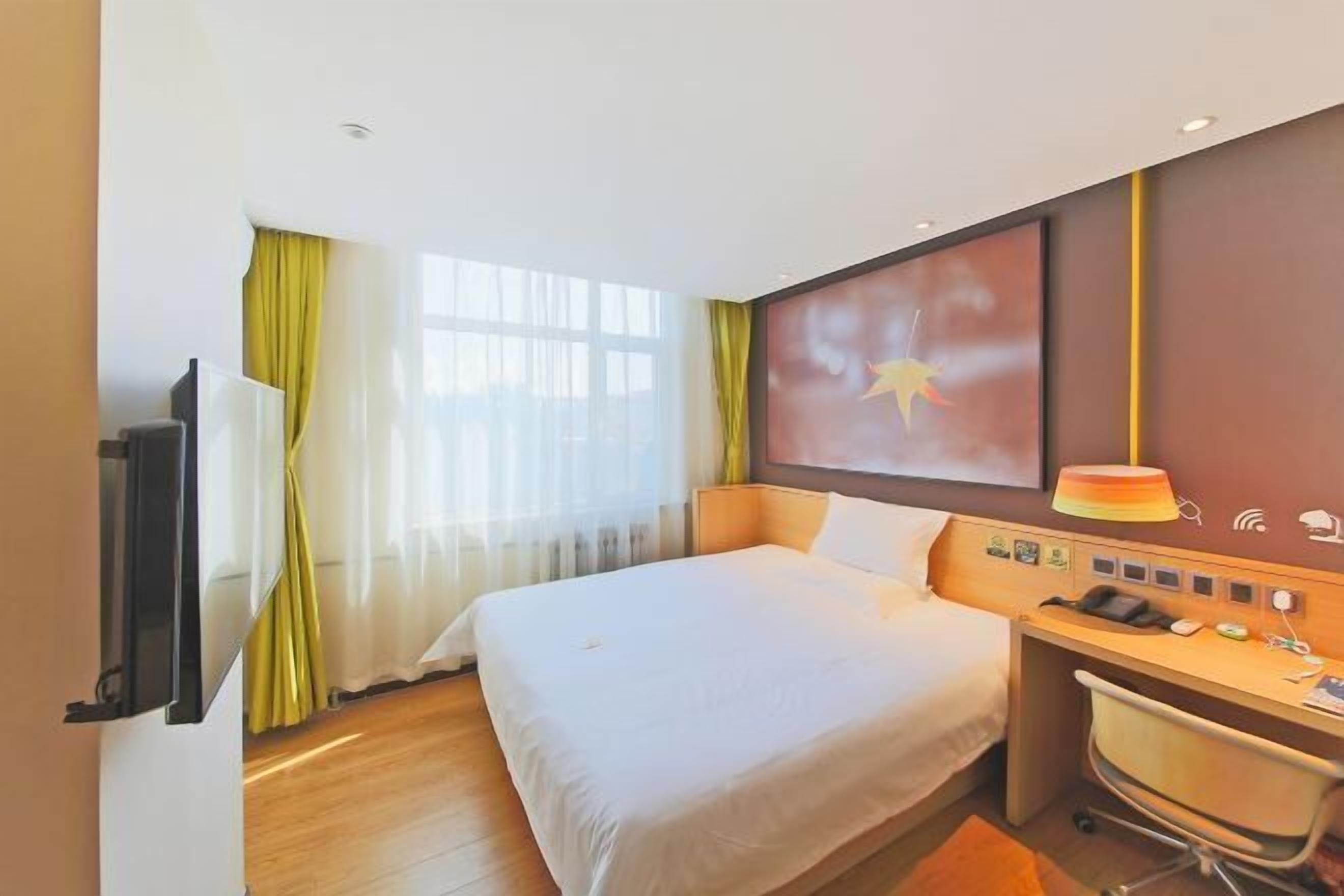 A hotel room with a bed, desk, chair, and a television.