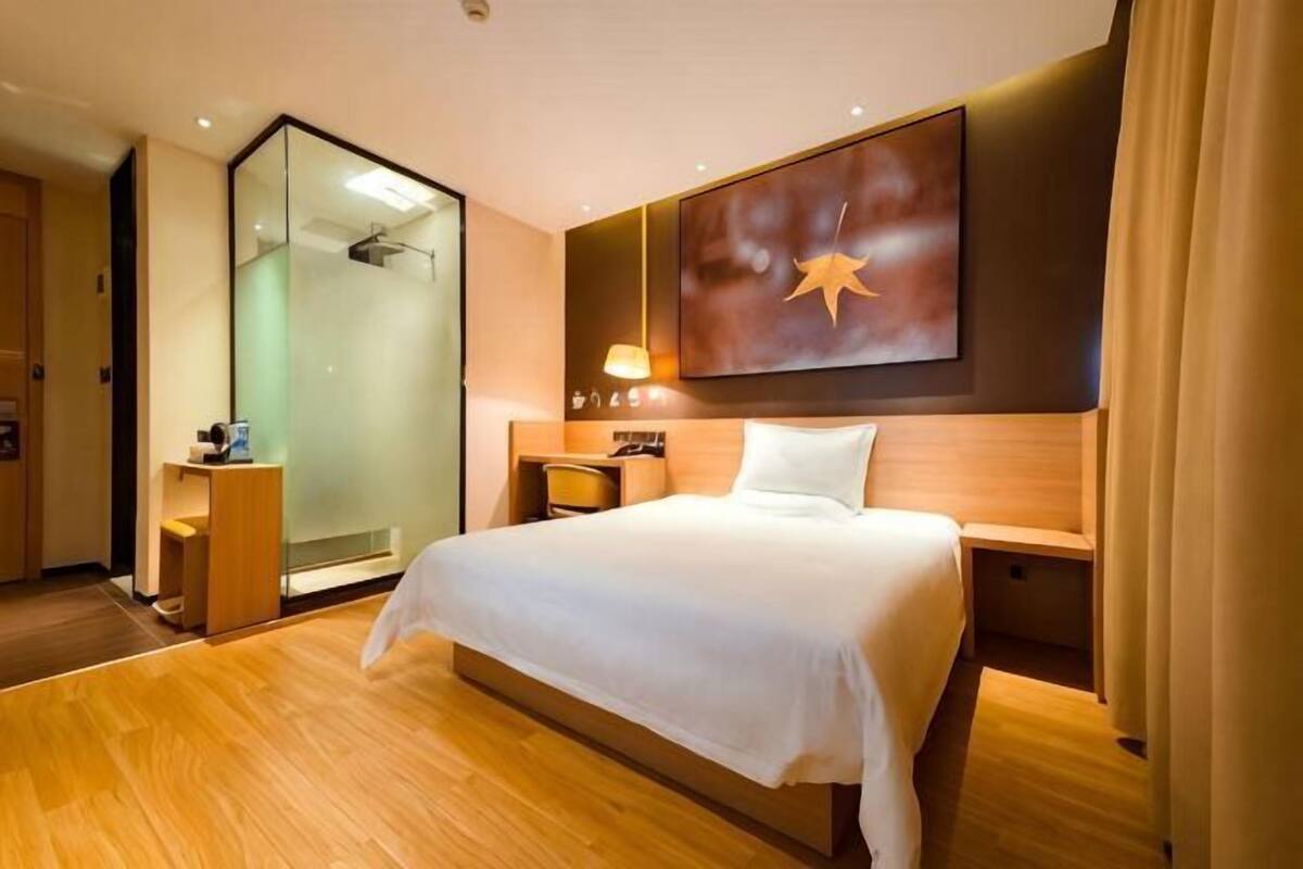 A hotel room with a bed, a desk, a mirror, and a shower.