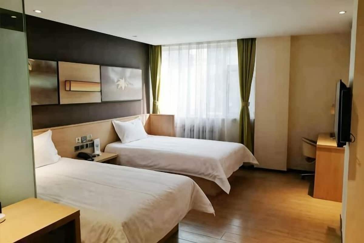 A hotel room with two beds, a desk, a TV, and a window with curtains.