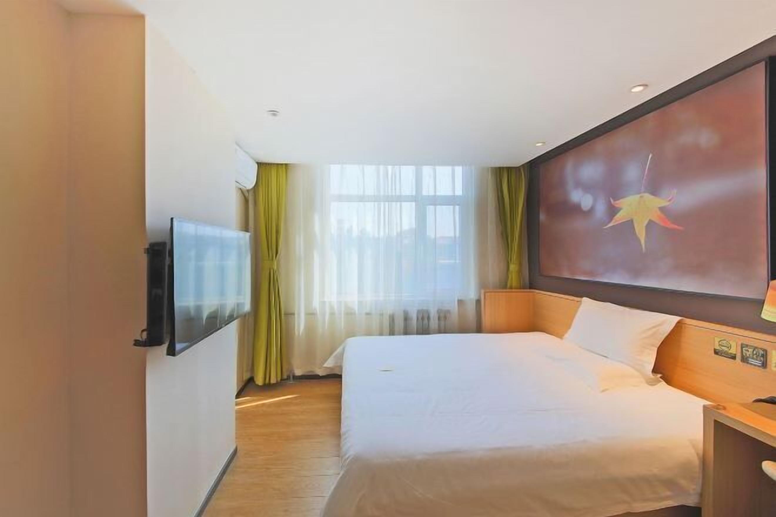 Une chambre d’hôtel avec un lit, un téléviseur fixé au mur, une fenêtre avec des rideaux et une décoration en forme d’étoile sur le mur.