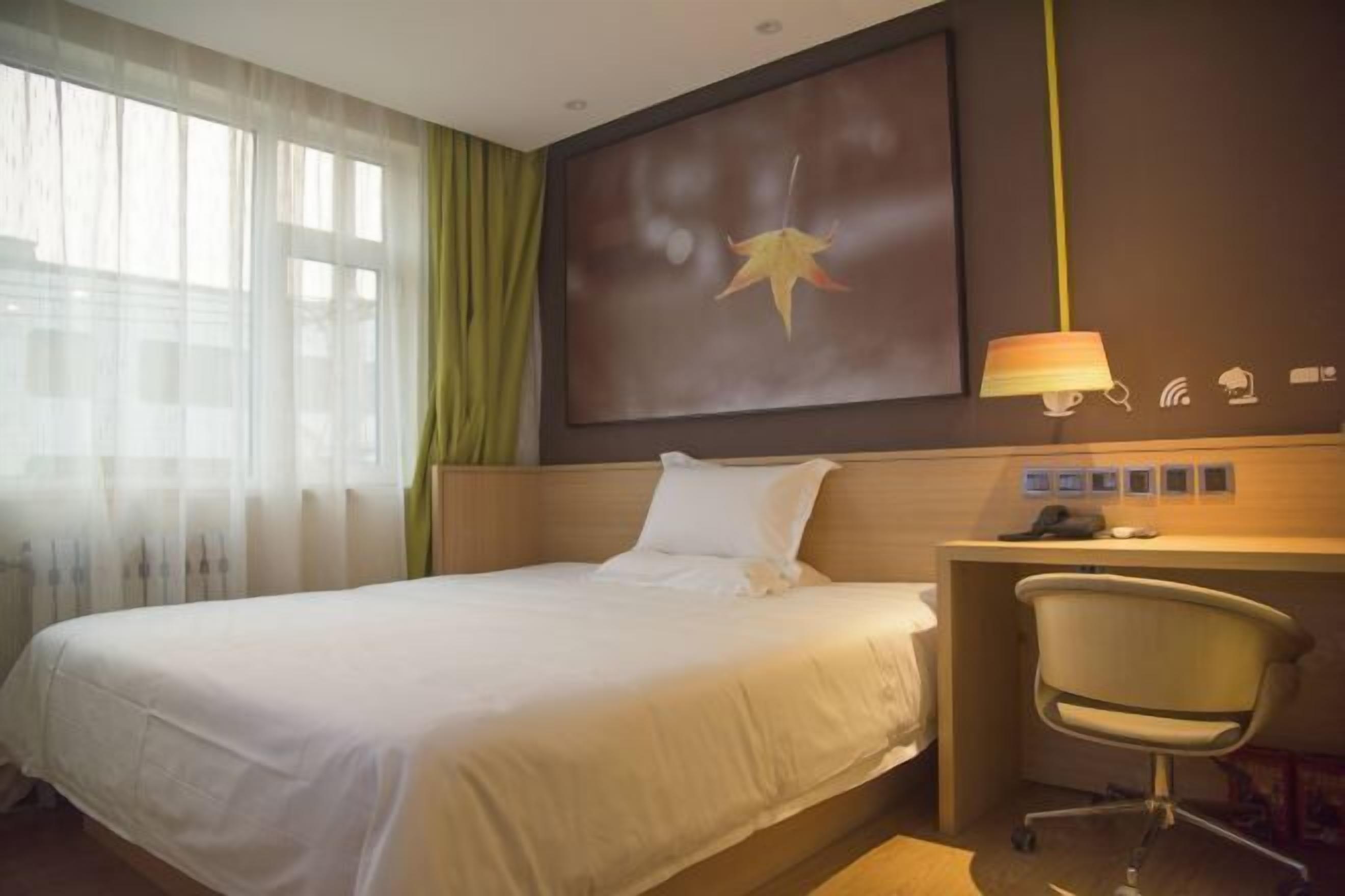 Une chambre d’hôtel comprenant un lit, un bureau avec une chaise, une lampe et une œuvre d’art accrochée au mur.
