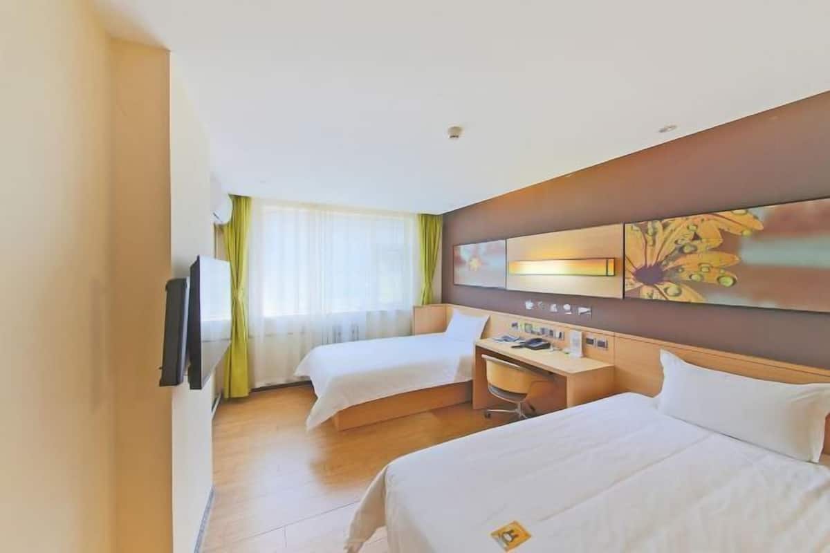 A hotel room with two beds, a desk, and a large window with curtains.