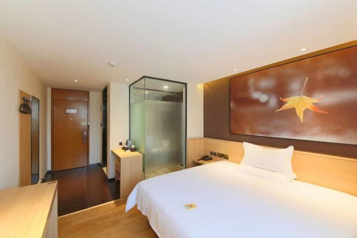 A hotel room with a bed, a desk, a glass partition, and a large wall-mounted artwork.