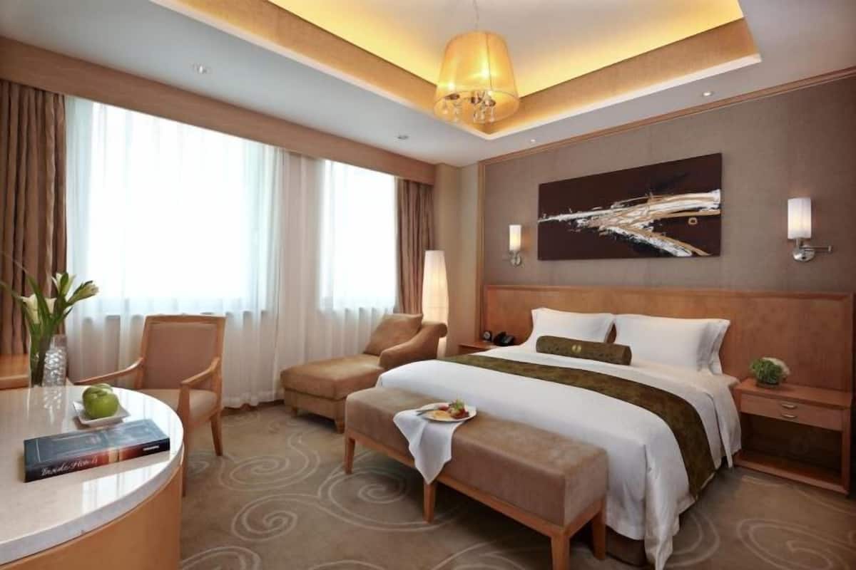 A hotel room with a large bed, a desk, a chair, and a window with curtains.