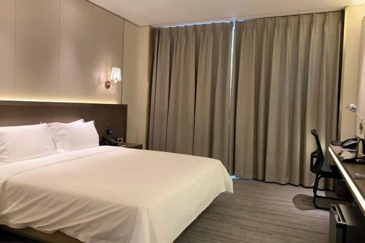 A hotel room with a bed, a desk, a chair, a lamp, and a curtain.