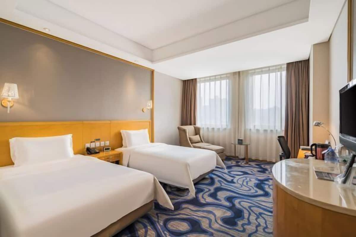 A hotel room with two beds, a desk, a chair, a TV, and a window with curtains.