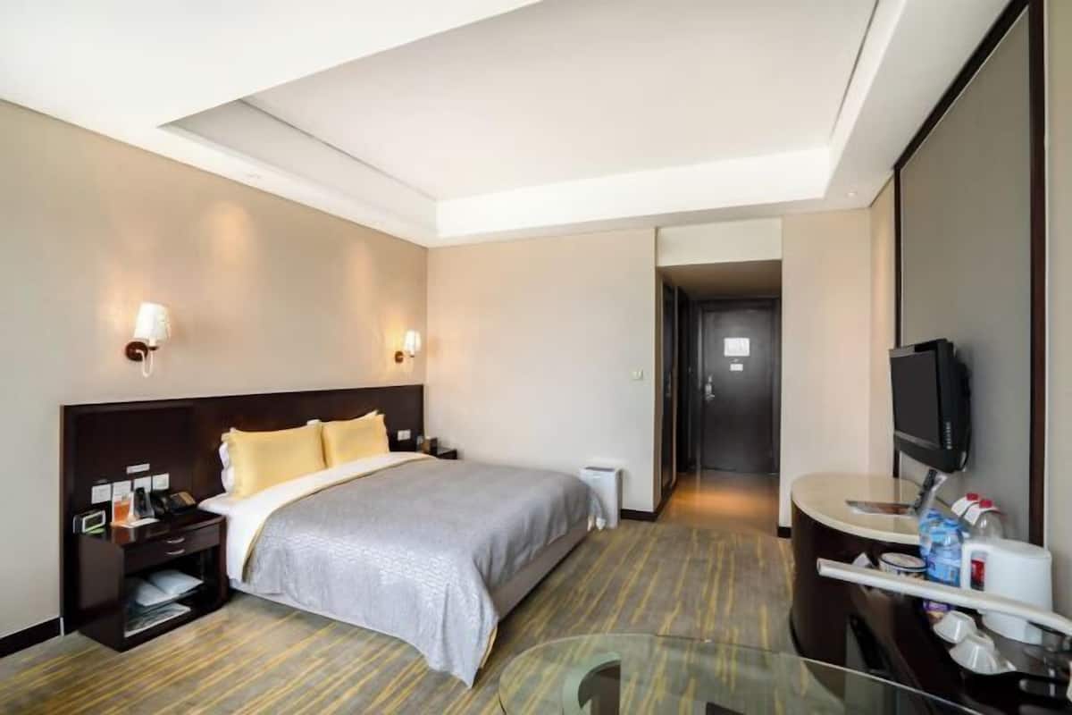 A hotel room with a bed, bedside tables, a TV, and a glass partition.