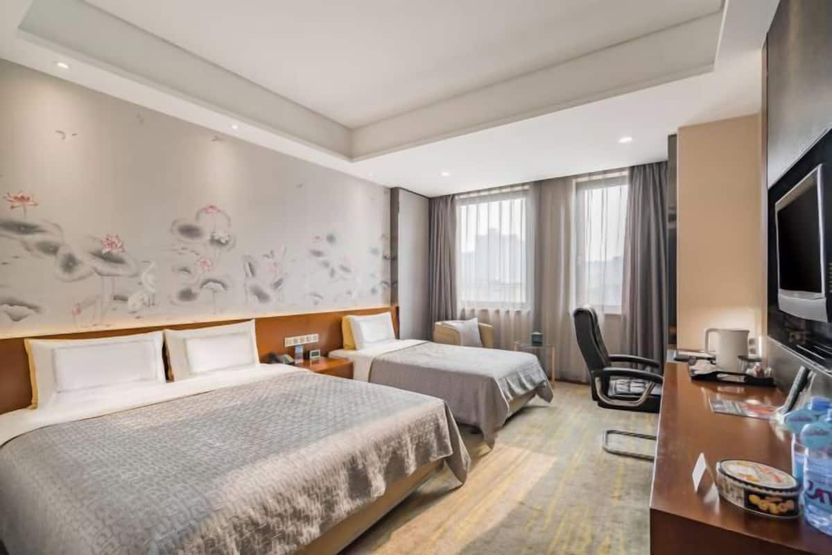 A hotel room with two beds, a desk, a television, and a wall with artwork.