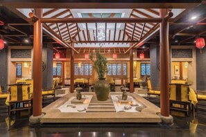 Un restaurante de estilo tradicional con un área de asientos central, pilares de madera y un jarrón grande con plantas.