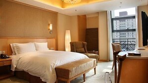 Habitación de hotel con una cama grande, un escritorio con silla, una lámpara y vista a la ciudad desde la ventana.