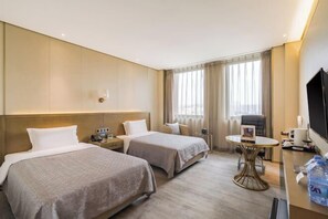 A hotel room with two beds, a desk, a chair, a TV, and a window with curtains.
