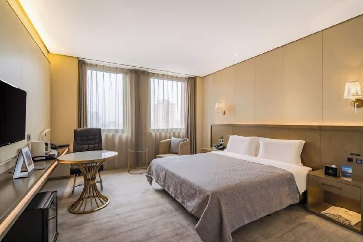 A hotel room with a bed, a desk, a chair, a TV, and a window with curtains.